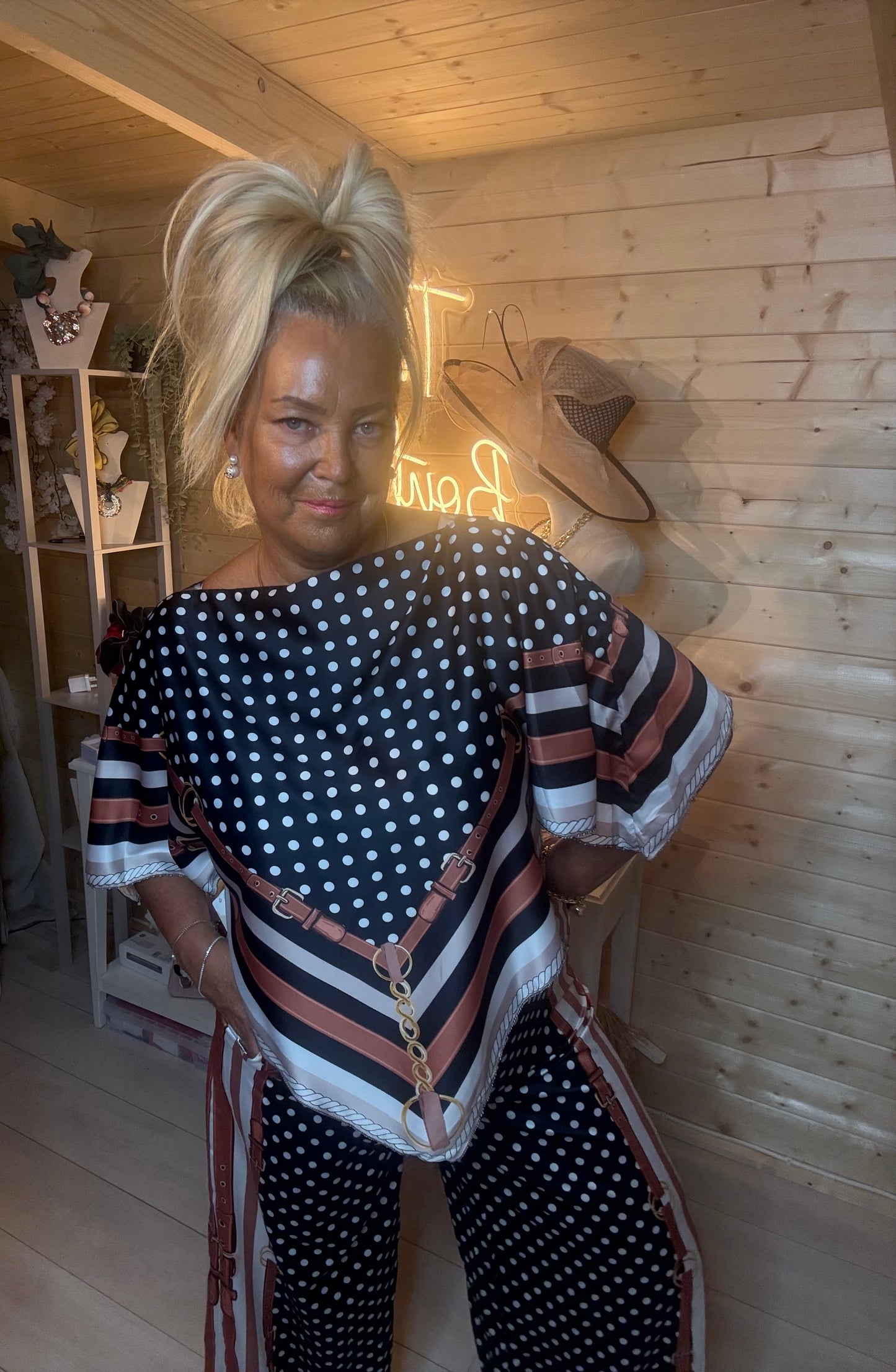 Rust terracotta polka dot scarf print co-ord set – full length front view showing batwing top with chevron scarf-print hem and matching wide-leg trousers styled with silver mules in boutique setting