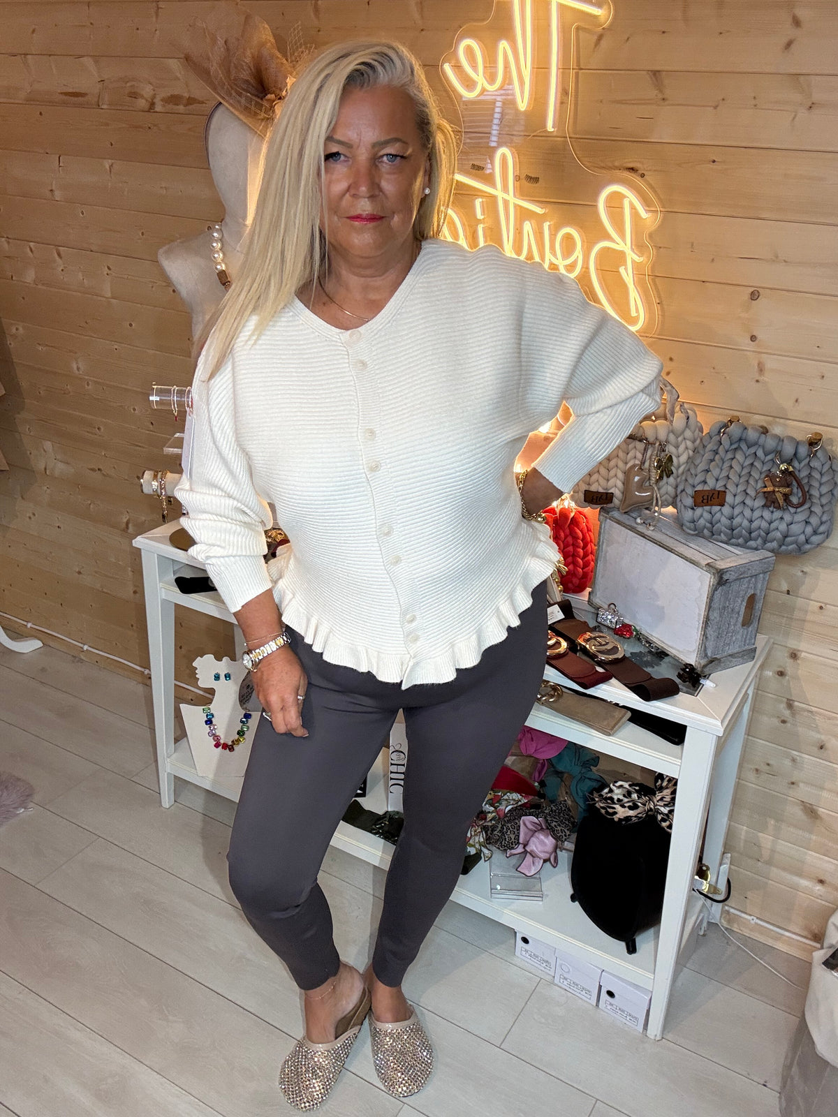 Cream ribbed cardigan with frilled hem styled over dark leggings and a patterned bow scarf