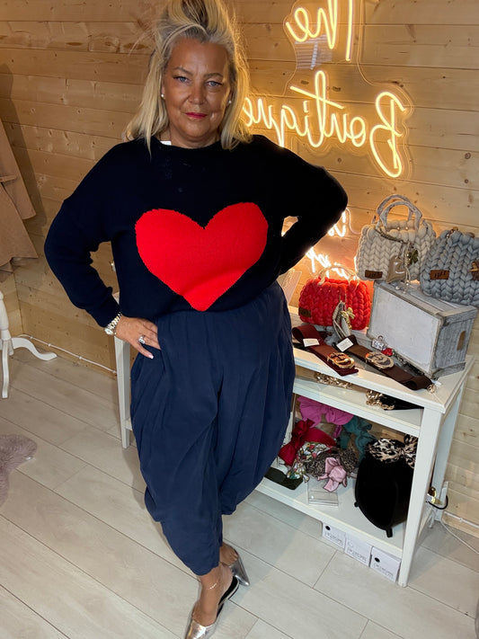 Full-length view of a model wearing a navy jumper with a large red heart, styled with navy trousers