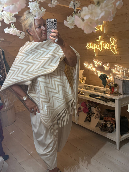 Alba oversized cream and white chevron patterned cape wrap with fringe trim, styled over cream trousers