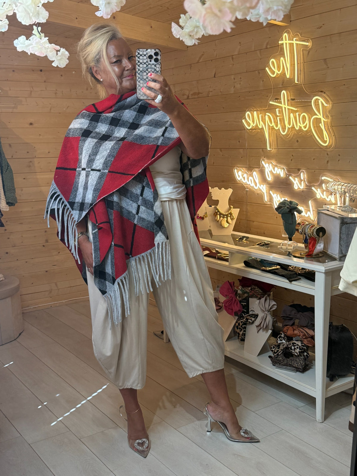 Roxie red, grey and black checked fringed cape wrap shown draped across shoulders with cream trousers