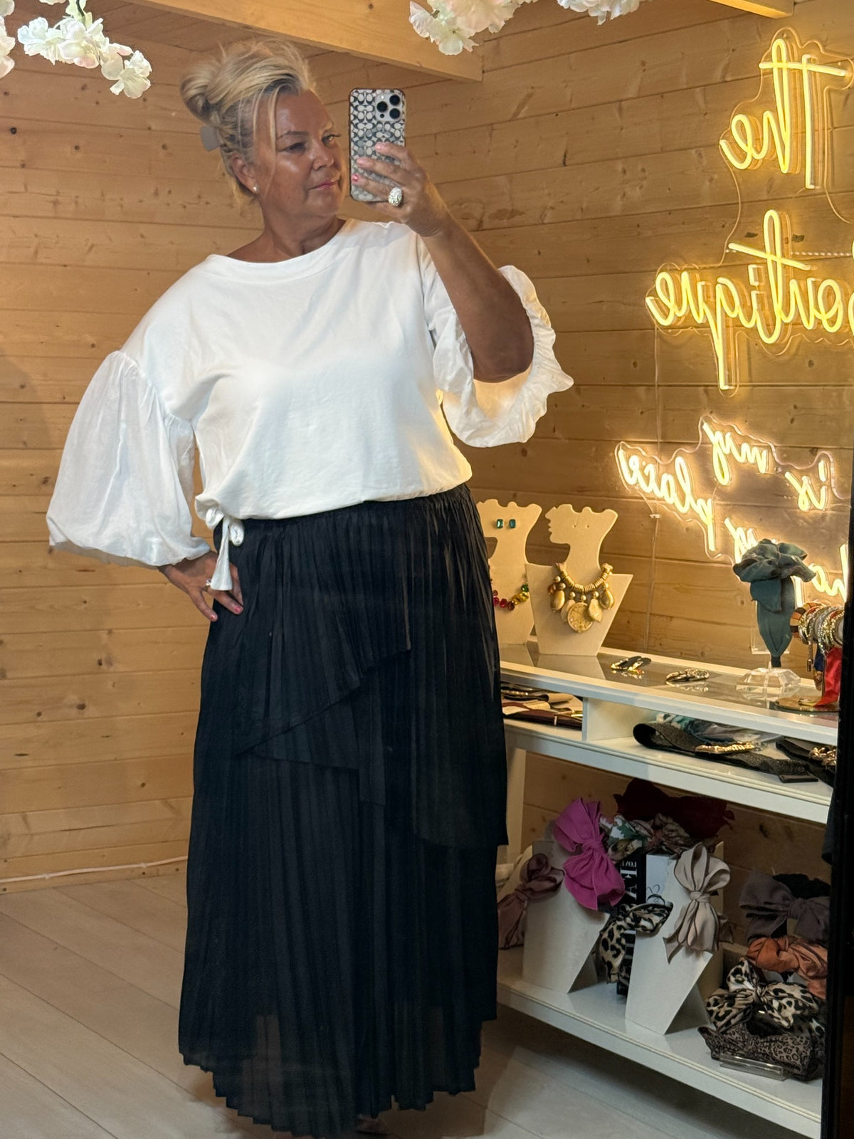 Front view of black layered pleated maxi skirt worn with white statement sleeve top