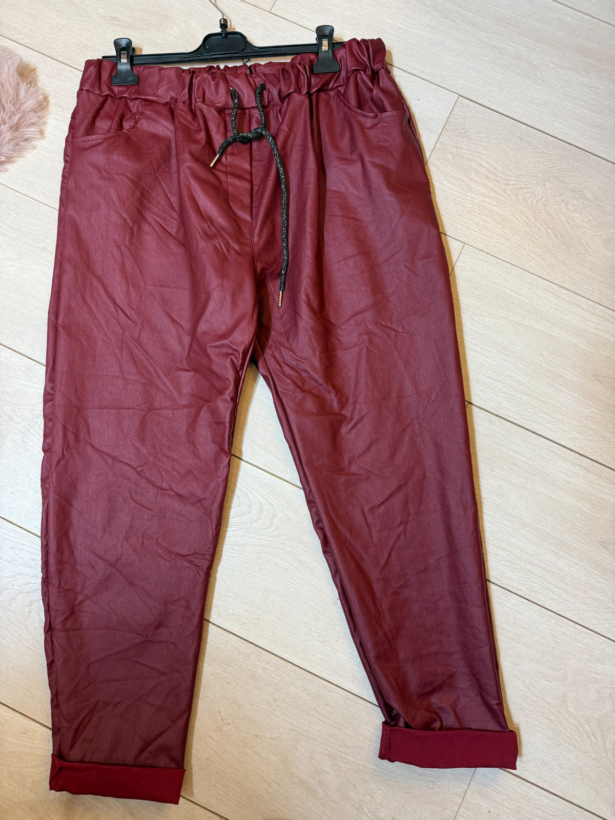 Burgundy faux leather look drawstring magic trousers with pockets and rolled hems laid flat